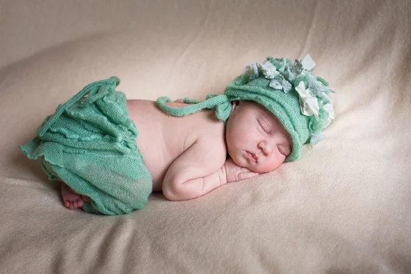 Sovande nyfödd flicka i en grön stickad trosor och hatt. — Stockfoto