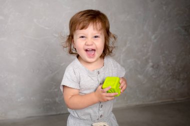 Küçük kız gri duvar arka plan üzerinde oyuncakla oynamak.