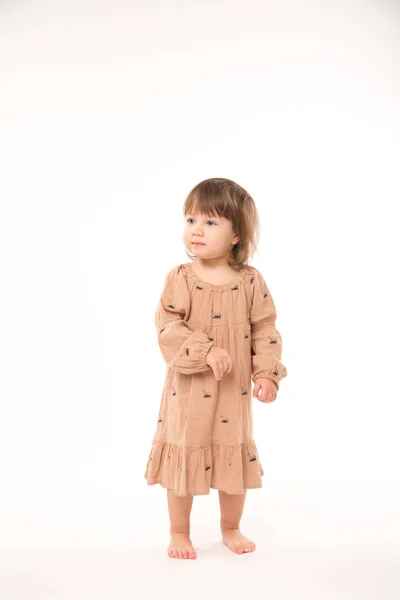 Schattig klein meisje in beige jurk geïsoleerd op witte achtergrond. — Stockfoto