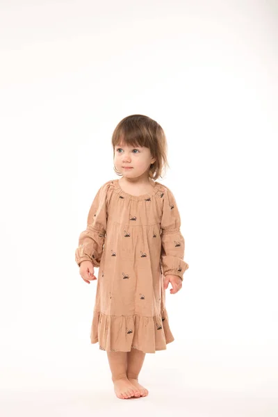 Söt liten flicka i beige klänning isolerade på vit bakgrund. — Stockfoto