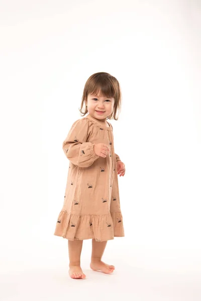 Schattig klein meisje in beige jurk geïsoleerd op witte achtergrond. — Stockfoto