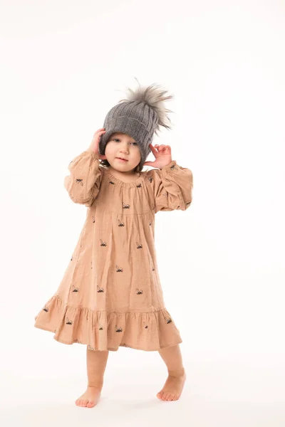 Schattig klein meisje in beige jurk in een grijze hoed geïsoleerd op witte achtergrond. — Stockfoto