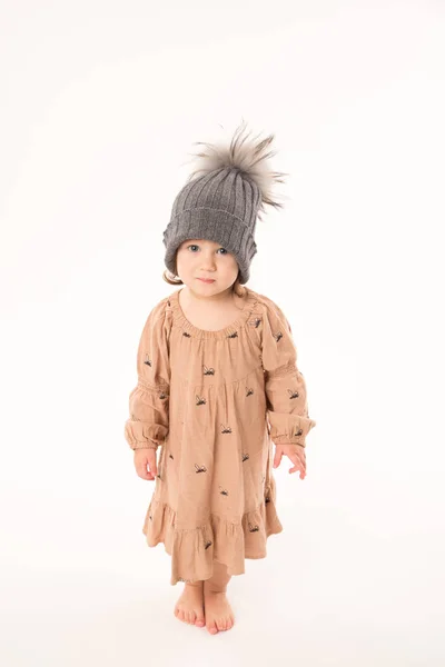 Милая маленькая девочка в бежевом платье в серой шляпе изолированы на белом фоне . — стоковое фото