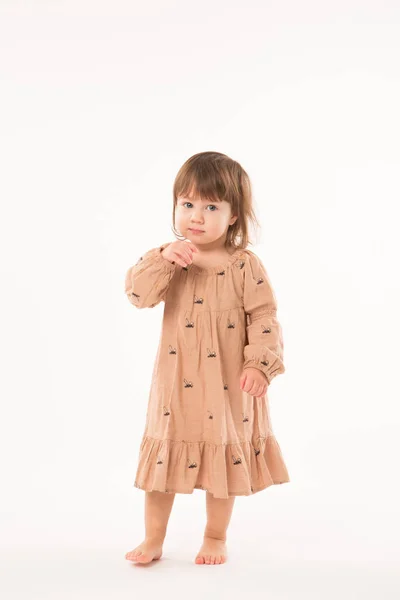 Schattig klein meisje in beige jurk geïsoleerd op witte achtergrond. Stockfoto