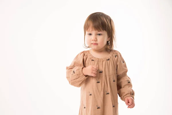 Schattig klein meisje in beige jurk geïsoleerd op witte achtergrond. Stockfoto