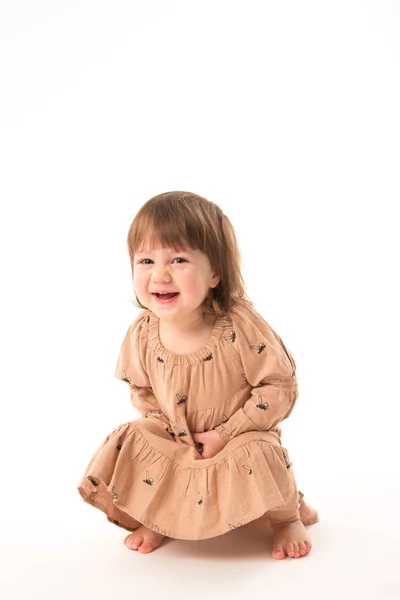 Schattig klein meisje in beige jurk geïsoleerd op witte achtergrond. Stockfoto