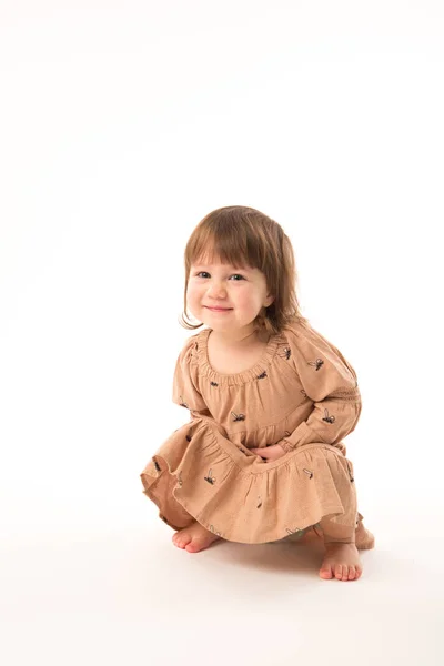Schattig klein meisje in beige jurk geïsoleerd op witte achtergrond. — Stockfoto