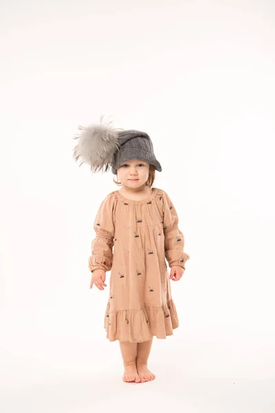 Carino bambina in abito beige in un cappello grigio isolato su sfondo bianco . Immagini Stock Royalty Free