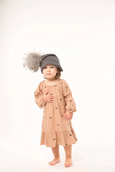 Carino bambina in abito beige in un cappello grigio isolato su sfondo bianco . Immagini Stock Royalty Free