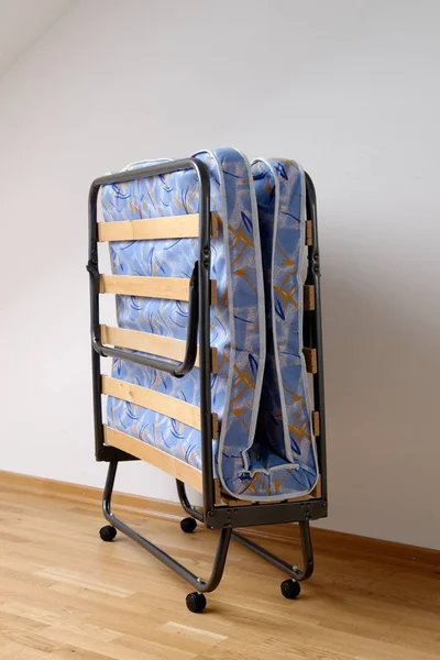 A folding bed in front of a white wall an a blue mattress