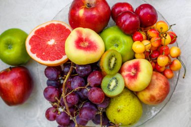 Şeftalili, kirazlı, greyfurtlu, elmalı, armutlu ve kivili cam bir tabak.