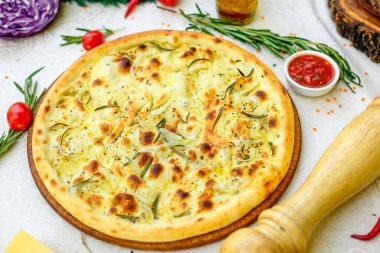 Tahta bir yüzeyde soğanlı ve fesleğenli sıcak pizza ve beyaz bir masada sebzeler.