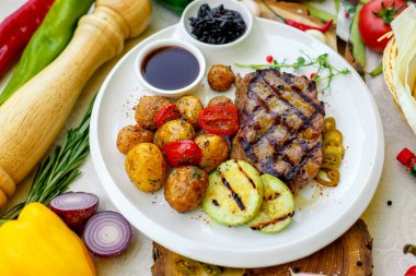Barbekü, ızgara sebzeli sulu biftek ve beyaz tabakta sos.