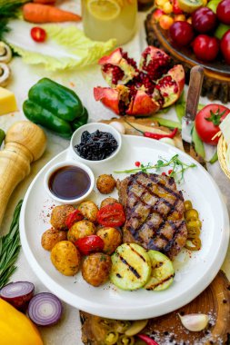 Barbekü, ızgara sebzeli sulu biftek ve beyaz tabakta sos.