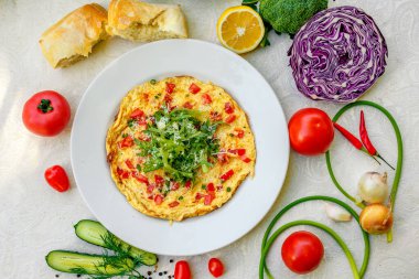 Yumurtalı omlet, kiraz domatesleri, peynir ve masasında beyaz bir masa örtüsü olan roka.