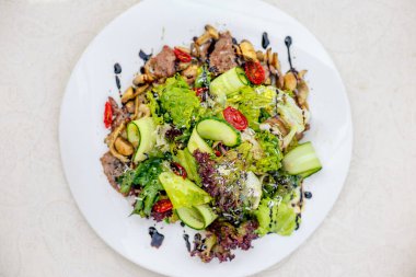 Masadaki beyaz tabakta etli, salatalıklı ve sebzeli salata.