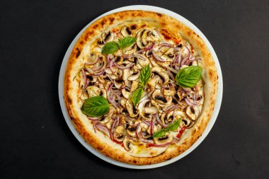 Siyah bir masada parmesanlı, mantarlı, soğanlı ve fesleğenli İtalyan pizzası.