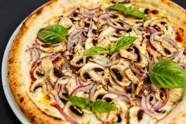 Siyah bir masada parmesanlı, mantarlı, soğanlı ve fesleğenli İtalyan pizzası.