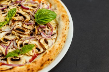 Siyah bir masada parmesanlı, mantarlı, soğanlı ve fesleğenli İtalyan pizzası.