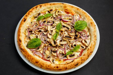 Siyah bir masada parmesanlı, mantarlı, soğanlı ve fesleğenli İtalyan pizzası.