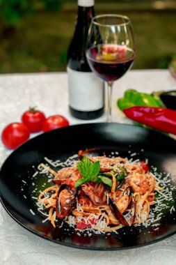 Parmesan peynirli İtalyan makarnası ve deniz ürünleri, ahtapot, karides ve midye ile beyaz bir masada siyah bir tabakta.