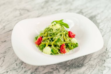 Beyaz tabakta peynirli ve sebzeli İtalyan makarnası.