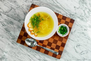 Tavuklu çorba, mantarlar ve beyaz tabakta bitkiler, güzel bir servis.