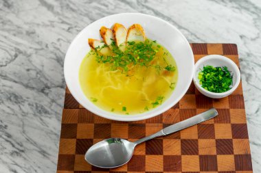 Tavuklu çorba, mantarlar ve beyaz tabakta bitkiler, güzel bir servis.