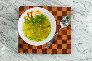 Tavuklu çorba, mantarlar ve beyaz tabakta bitkiler, güzel bir servis.