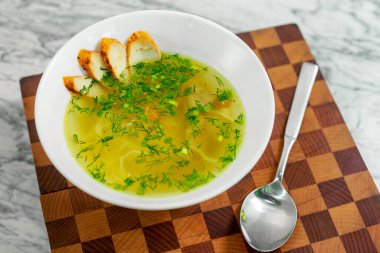 Tavuklu çorba, mantarlar ve beyaz tabakta bitkiler, güzel bir servis.