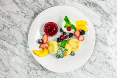 Beyaz tabakta meyve ve reçelli süzme peynir krepleri.