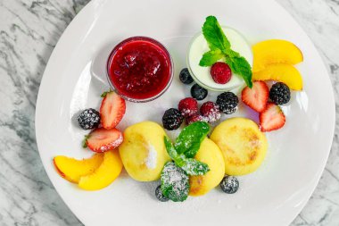 Beyaz tabakta meyve ve reçelli süzme peynir krepleri.