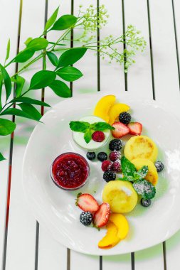 Beyaz tabakta meyve ve reçelli süzme peynir krepleri.