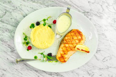 Kızarmış somon balığı, patates püresi ve beyaz tabakta limon.