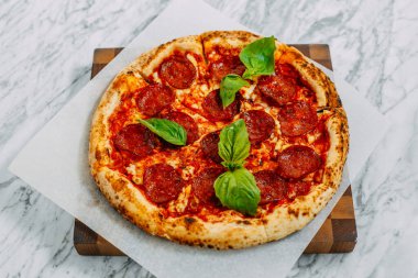 İtalyan pizzası, mozzarella peyniri ve fesleğen ile mermer bir masada.