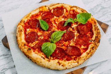 İtalyan pizzası, mozzarella peyniri ve fesleğen ile mermer bir masada.