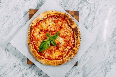 İtalyan pizzası, mozzarella peyniri ve fesleğen ile mermer bir masada.