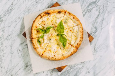 İtalyan pizzası, mozzarella peyniri ve fesleğen ile mermer bir masada.