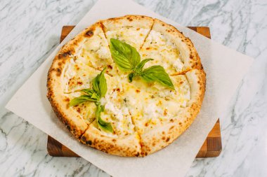 İtalyan pizzası, mozzarella peyniri ve fesleğen ile mermer bir masada.