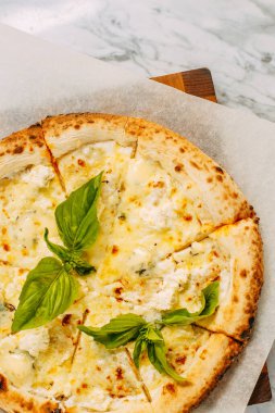 İtalyan pizzası, mozzarella peyniri ve fesleğen ile mermer bir masada.