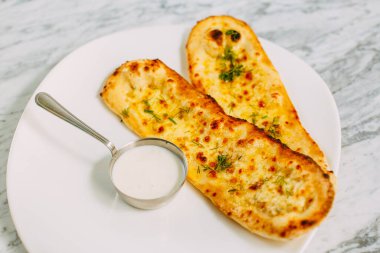 Peynirli ve otlu sarımsaklı ekmek, mermer bir masada sos.