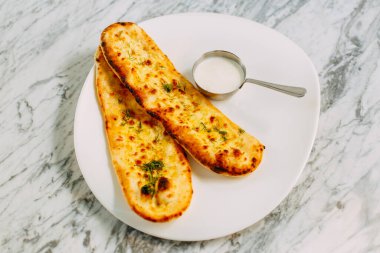 Peynirli ve otlu sarımsaklı ekmek, mermer bir masada sos.