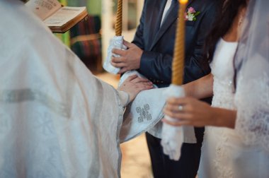 Gelin ve damadın elleri düğün havlularını bağladı. Rahip gelinin el havlusunu bağlar. Kilisedeki genç çiftlerin elleri. Kilise töreninde el ele tutuşan çift. Düğün günü..