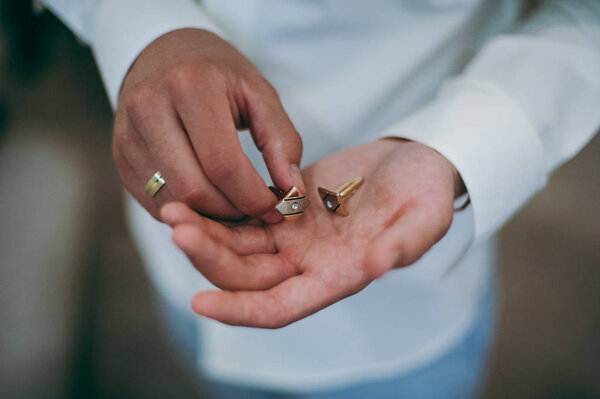 Жених закрепляет запонку на рукаве рубашки крупным планом
