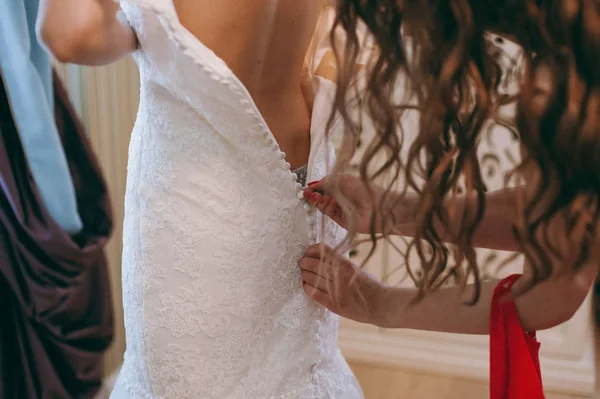 Fashionabla brudtärnor klänningar hjälpte slitage rosett på baksidan av bröllop klänning bruden. Morgonen bröllopsdag. — Stockfoto