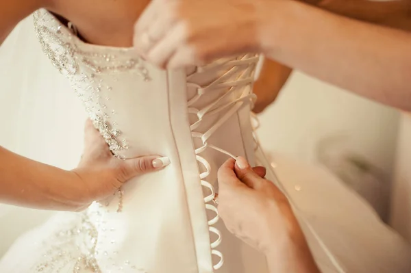 Fashionable bridesmaids dresses helped wear bow on back of wedding dress bride. Morning wedding day. — Stock Photo, Image