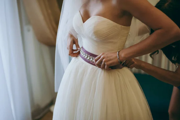 Fashionable bridesmaids dresses helped wear bow on back of wedding dress bride. Morning wedding day. — Stock Photo, Image