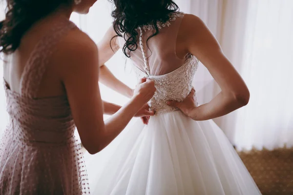 Fashionable bridesmaids dresses helped wear bow on back of wedding dress bride. Morning wedding day. — Stock Photo, Image