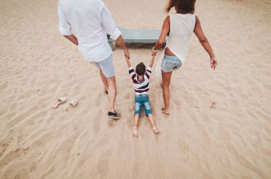 Mutlu genç aile sahilde koşup gün batımında zıplıyor.