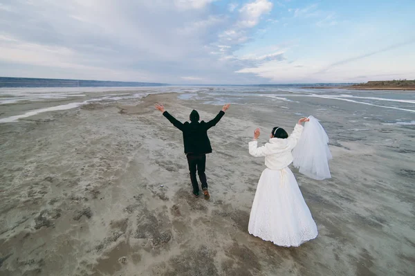 Couple de mariage sur une promenade mariée et marié champ de mer coucher de soleil architecture herbe sable — Photo